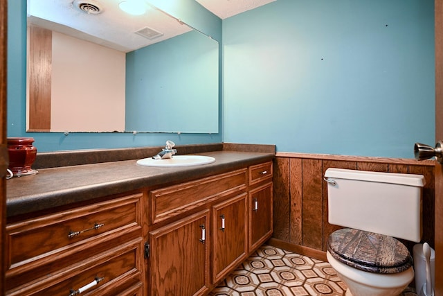 bathroom with wooden walls, vanity, a textured ceiling, and toilet