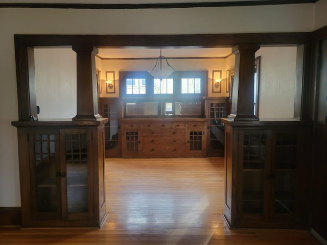 interior space featuring decorative columns, wood-type flooring, and decorative light fixtures