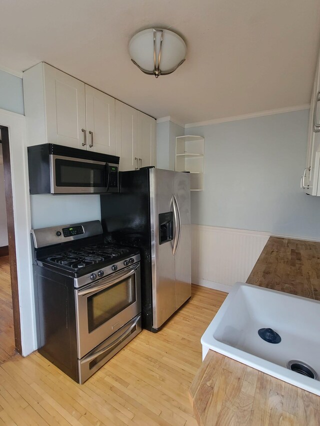 kitchen with stainless steel appliances, white cabinetry, light hardwood / wood-style floors, and sink