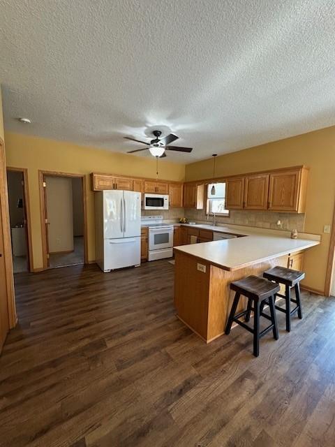 kitchen with white appliances, dark wood-type flooring, a textured ceiling, a kitchen bar, and kitchen peninsula