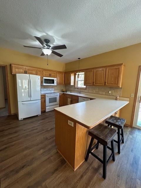 kitchen with dark hardwood / wood-style flooring, kitchen peninsula, decorative light fixtures, white appliances, and a breakfast bar