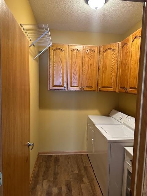 laundry room with washing machine and clothes dryer, cabinets, dark wood-type flooring, and a textured ceiling