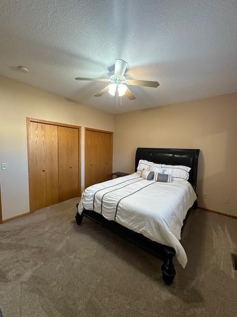 carpeted bedroom with ceiling fan, a textured ceiling, and two closets