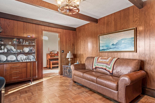 living room with beam ceiling, wood walls, a textured ceiling, and an inviting chandelier