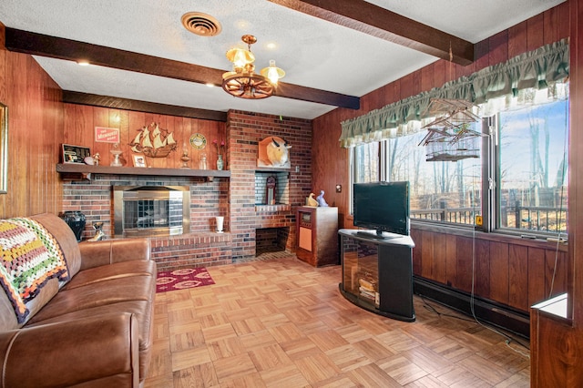 living room featuring a brick fireplace, a textured ceiling, a notable chandelier, beamed ceiling, and wood walls