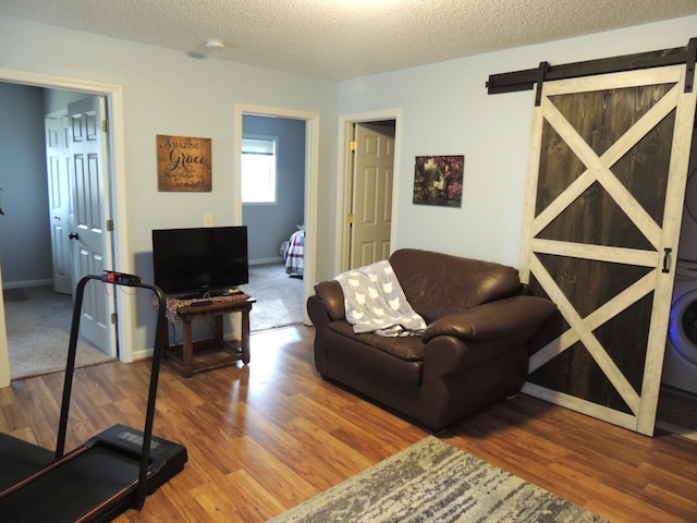 living room featuring stacked washer / drying machine, a barn door, wood-type flooring, and a textured ceiling