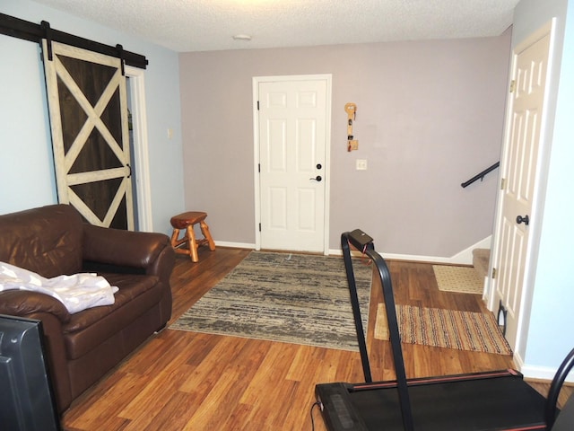 living area with a barn door, a textured ceiling, baseboards, and wood finished floors