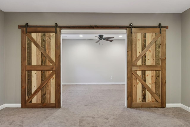 empty room featuring carpet floors, ceiling fan, and a barn door