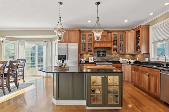 kitchen featuring stainless steel appliances, sink, custom range hood, a kitchen island, and pendant lighting