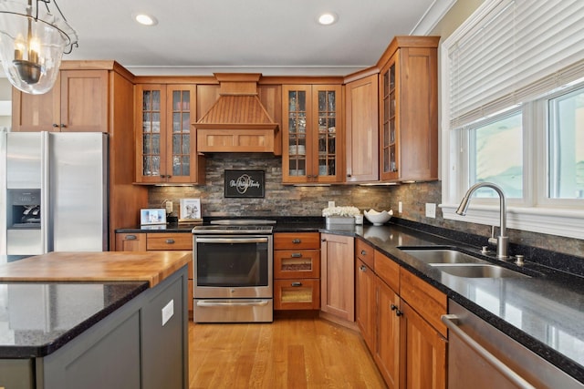 kitchen with dark stone countertops, stainless steel appliances, premium range hood, pendant lighting, and sink