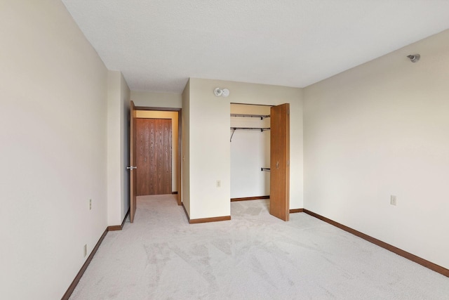 unfurnished bedroom featuring a textured ceiling, light carpet, baseboards, a spacious closet, and a closet