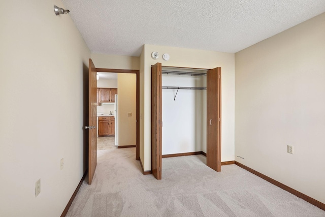 unfurnished bedroom with a closet, baseboards, a textured ceiling, and light colored carpet