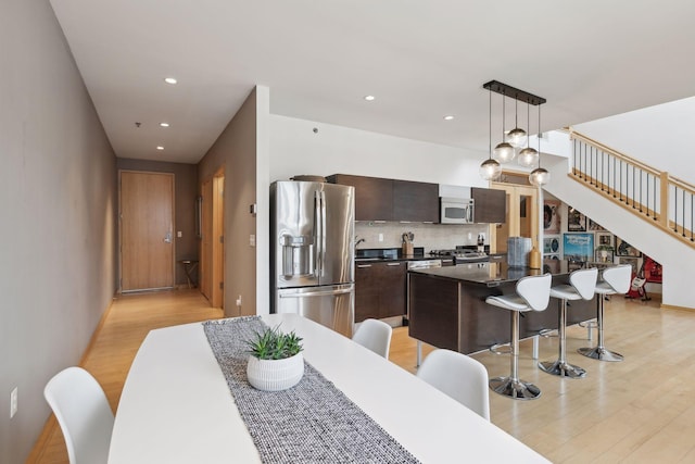 kitchen featuring appliances with stainless steel finishes, a breakfast bar area, dark brown cabinetry, decorative light fixtures, and a center island