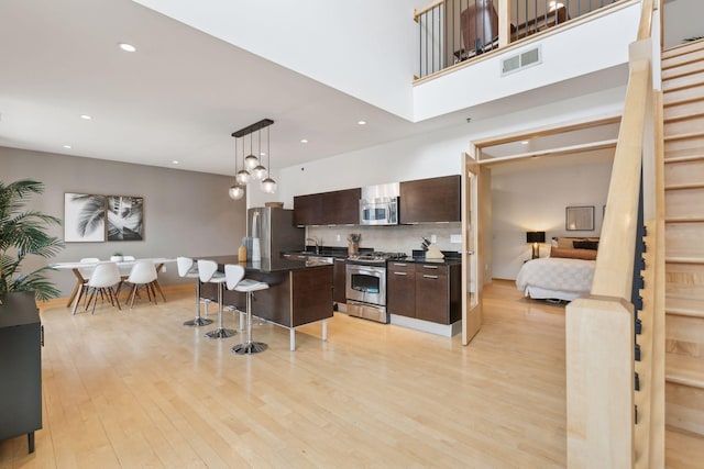 kitchen with a center island with sink, stainless steel appliances, decorative light fixtures, dark brown cabinets, and a kitchen bar