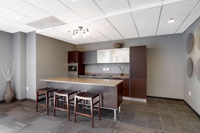 kitchen featuring dark tile patterned floors, sink, oven, a paneled ceiling, and a kitchen breakfast bar