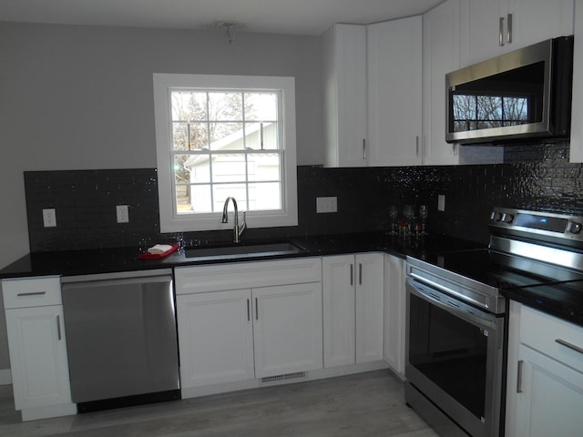 kitchen featuring white cabinetry, sink, stainless steel appliances, light hardwood / wood-style floors, and decorative backsplash