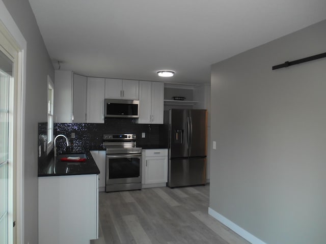 kitchen with backsplash, light wood-type flooring, stainless steel appliances, sink, and white cabinetry