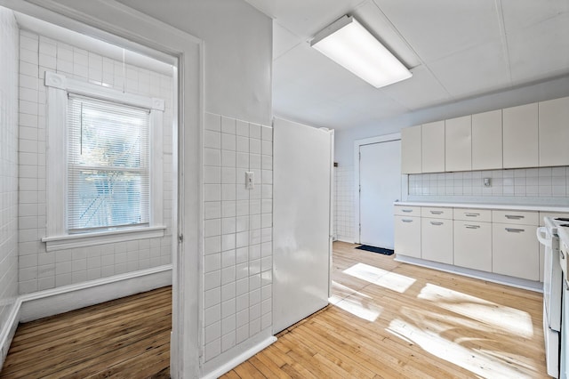 kitchen with white range, backsplash, light hardwood / wood-style floors, white cabinets, and tile walls