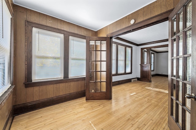 empty room with french doors, light hardwood / wood-style floors, crown molding, and wooden walls