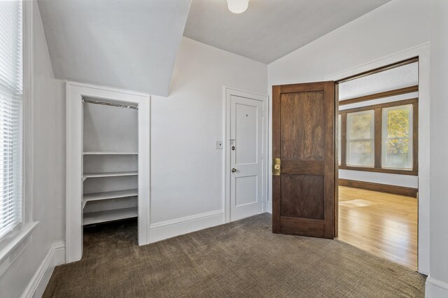 unfurnished bedroom with dark hardwood / wood-style floors, a walk in closet, and vaulted ceiling