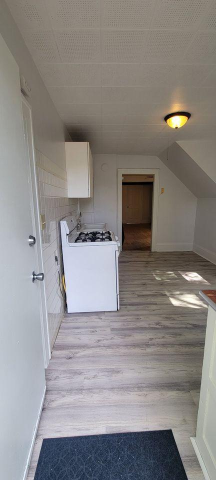 kitchen featuring white gas stove, white cabinetry, light wood-type flooring, and vaulted ceiling