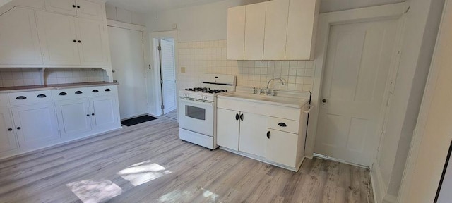 kitchen featuring sink, white gas range oven, decorative backsplash, light wood-type flooring, and white cabinetry