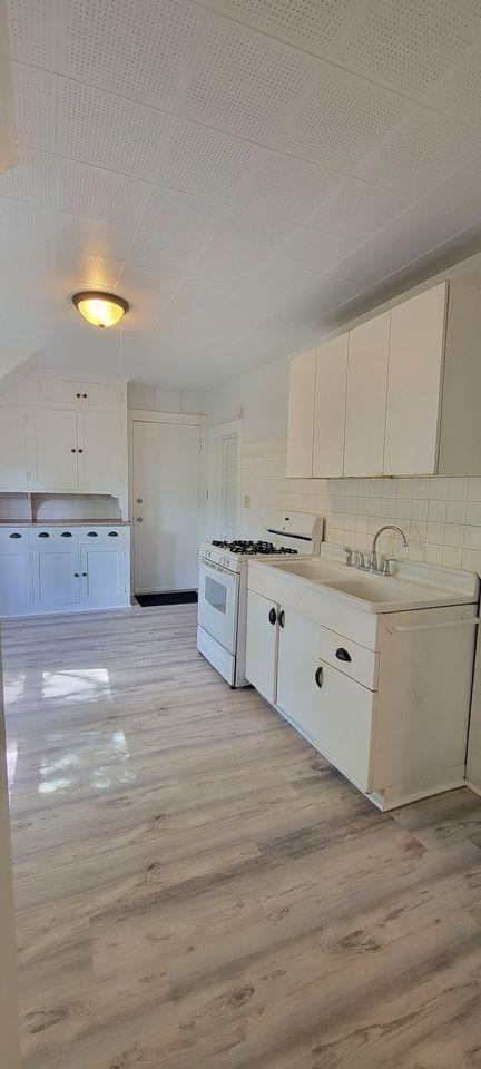 kitchen featuring backsplash, white cabinetry, light wood-type flooring, and white gas range oven