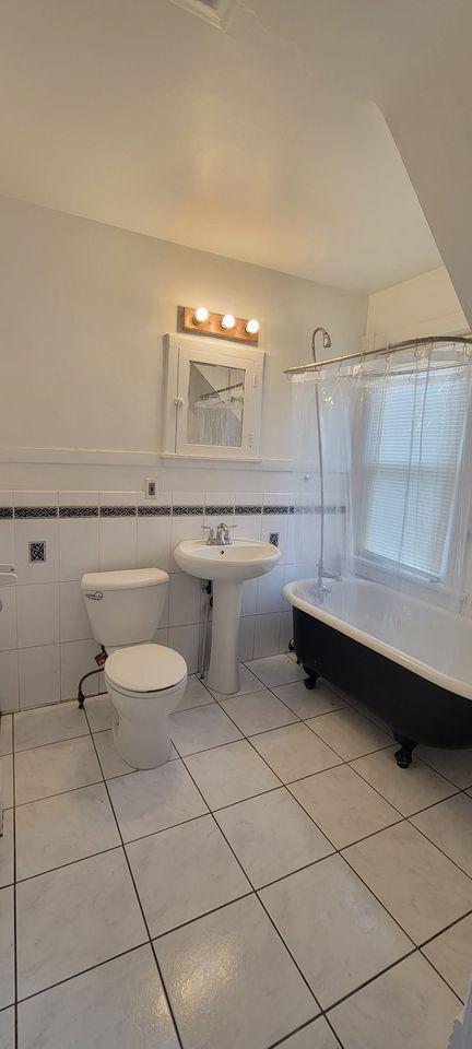 bathroom featuring tile patterned floors, a bathtub, sink, tile walls, and toilet