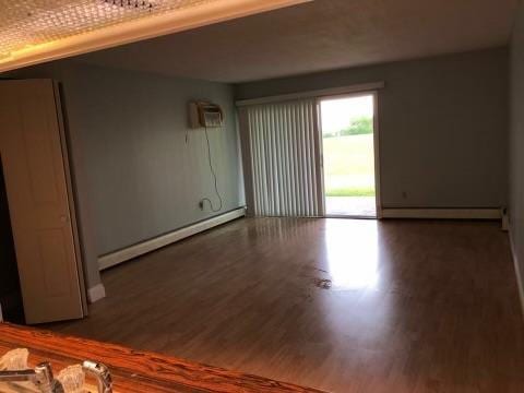 spare room with an AC wall unit, dark hardwood / wood-style flooring, and a baseboard heating unit