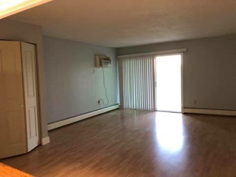 empty room with a baseboard radiator, a wall unit AC, and hardwood / wood-style flooring