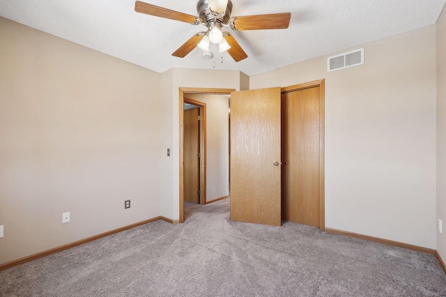 unfurnished bedroom featuring ceiling fan, a closet, light colored carpet, and a textured ceiling