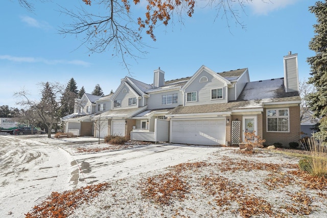 shingle-style home with a garage, brick siding, driveway, and a chimney