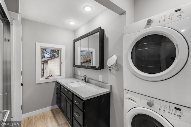 laundry room with sink, stacked washer and clothes dryer, and light hardwood / wood-style flooring