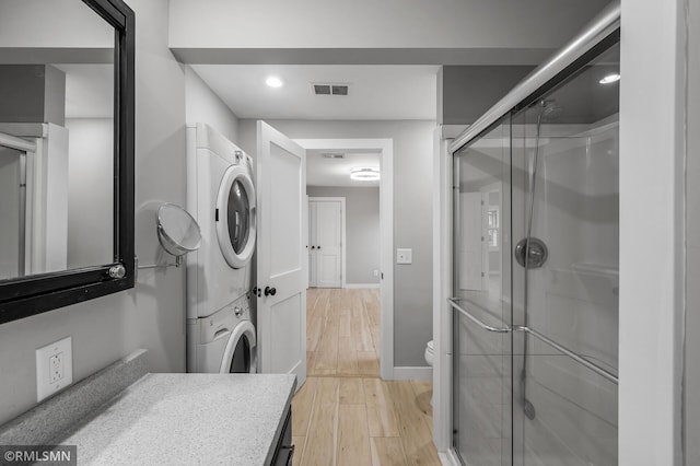 bathroom featuring stacked washing maching and dryer, vanity, a shower with door, wood-type flooring, and toilet