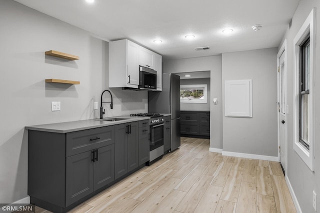 kitchen with gray cabinetry, white cabinets, sink, light hardwood / wood-style flooring, and stainless steel appliances