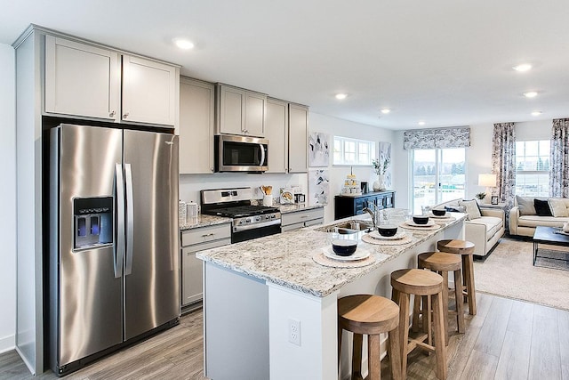 kitchen featuring a kitchen bar, light stone counters, stainless steel appliances, sink, and light hardwood / wood-style flooring