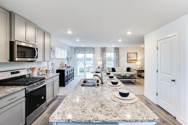 kitchen with a center island with sink, light wood-type flooring, sink, and appliances with stainless steel finishes