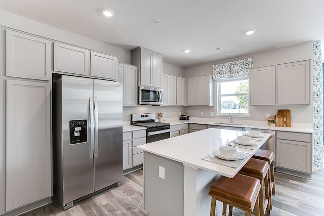 kitchen featuring a kitchen breakfast bar, stainless steel appliances, sink, light hardwood / wood-style flooring, and a kitchen island