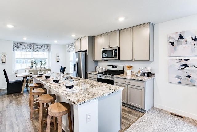 kitchen with hardwood / wood-style flooring, gray cabinets, stainless steel appliances, and a breakfast bar area