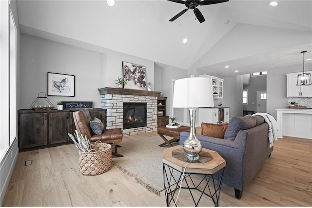 living room with a fireplace, light wood-type flooring, high vaulted ceiling, and ceiling fan