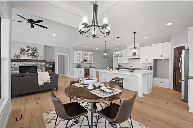 dining room with light wood-type flooring, ceiling fan with notable chandelier, crown molding, sink, and a fireplace