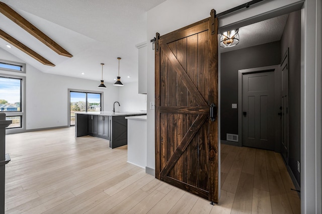 kitchen featuring pendant lighting, a kitchen island with sink, lofted ceiling with beams, a barn door, and light hardwood / wood-style floors