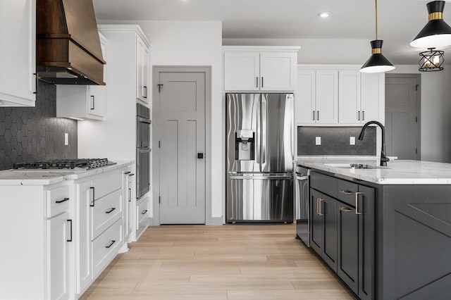 kitchen with appliances with stainless steel finishes, custom exhaust hood, sink, white cabinetry, and hanging light fixtures