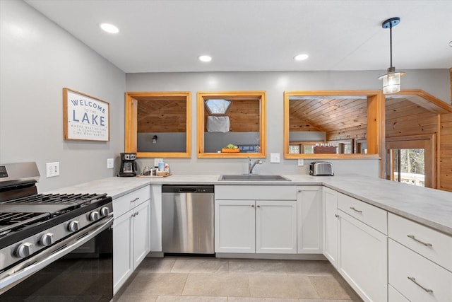 kitchen featuring white cabinets, sink, wooden walls, decorative light fixtures, and stainless steel appliances