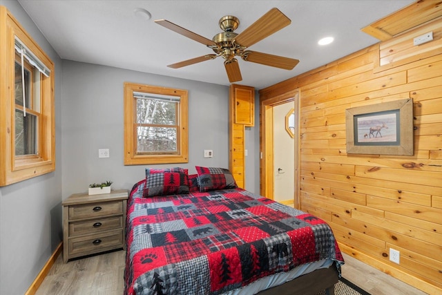 bedroom with ceiling fan, wood walls, and light hardwood / wood-style flooring