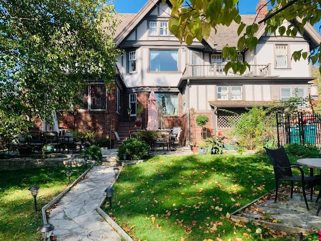 rear view of house featuring brick siding, a yard, a balcony, and fence