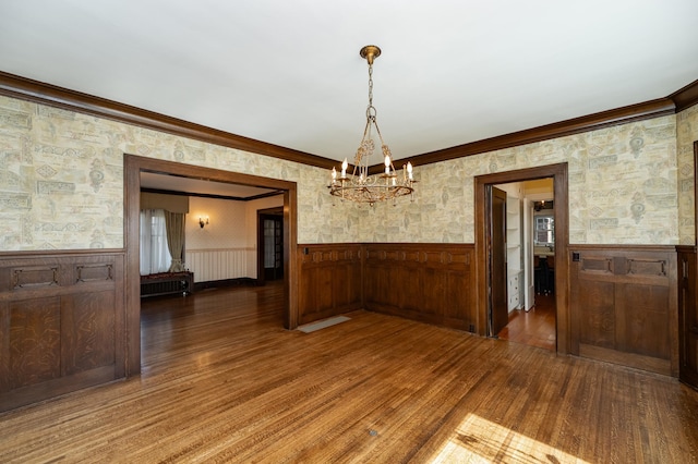 empty room featuring ornamental molding, wood finished floors, wainscoting, and wallpapered walls