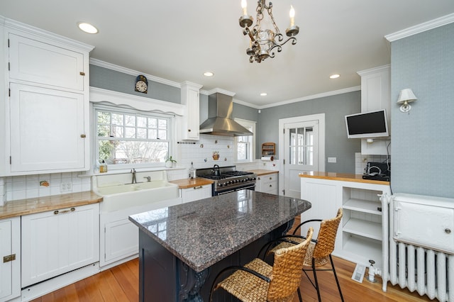 kitchen featuring a sink, high end stove, white cabinets, and wall chimney range hood