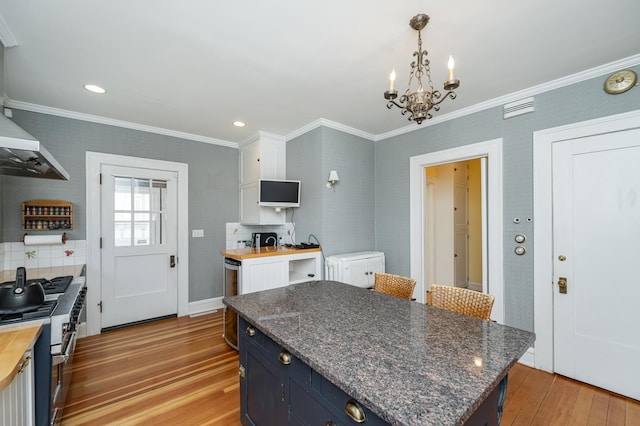 kitchen featuring ornamental molding, hanging light fixtures, butcher block countertops, light wood-style floors, and blue cabinets