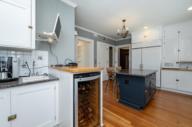 kitchen featuring white cabinets, beverage cooler, white microwave, and a sink